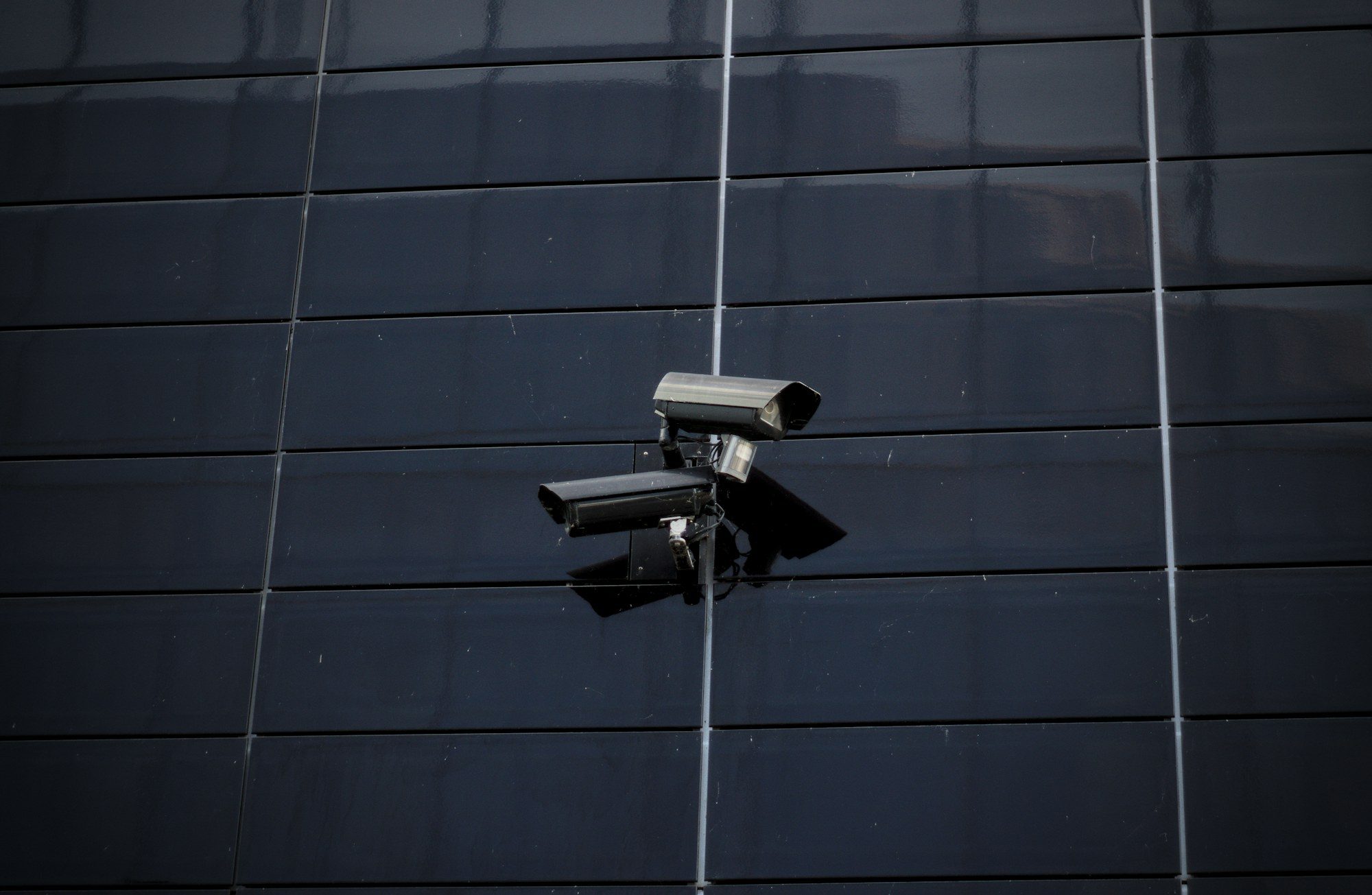 Two box cameras mounted on a dark panelled facade